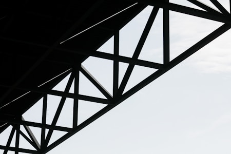 Geometric steel structure with intersecting beams against a light sky background.