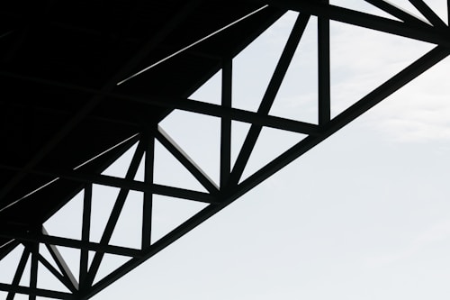 Geometric steel structure with intersecting beams against a light sky background.