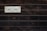 A wooden wall with horizontal planks features a vintage-style rectangular sign displaying the word 'Welcome' in bold black letters. The background of the sign is off-white with a decorative border in a rusty metal frame.