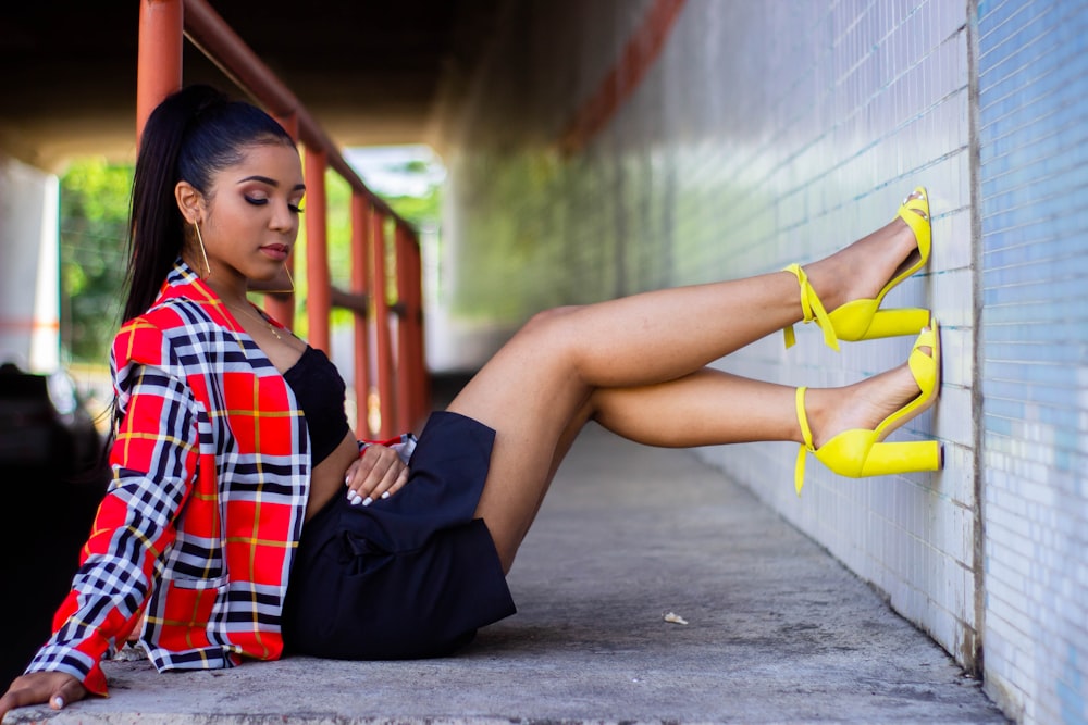 woman in red and blue plaid shirt and black skirt sitting on concrete pathway