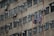 A tall, beige apartment building with multiple identical windows, each equipped with air conditioning units. Clothes are hung to dry on clotheslines outside several windows, adding a sense of daily life to the scene.