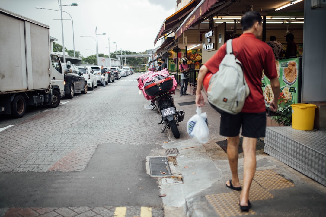 man in red and white shirt and black shorts standing on sidewalk during daytime