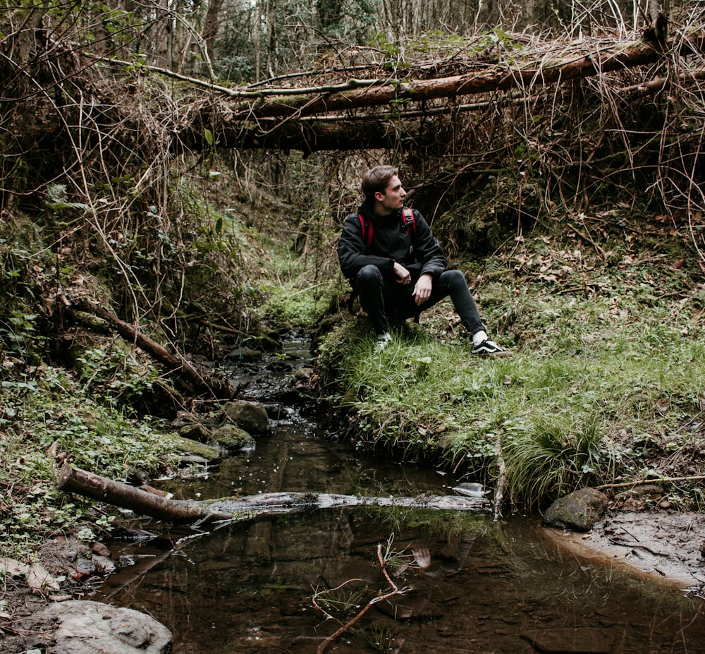 woman in black jacket sitting on rock near river during daytime