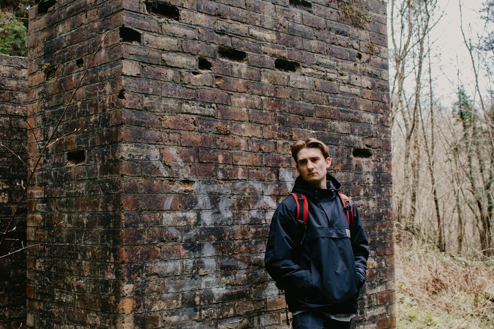man in black jacket standing beside brick wall