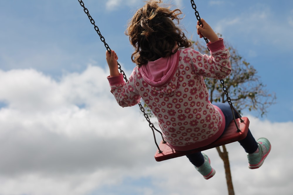 girl in pink and white polka dot long sleeve shirt riding swing during daytime