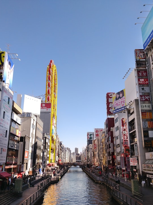 cars on road between high rise buildings during daytime in Dotombori Glico Sign Japan