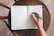 A hand holding a sleek ballpen, poised above a blank page in a notebook.
