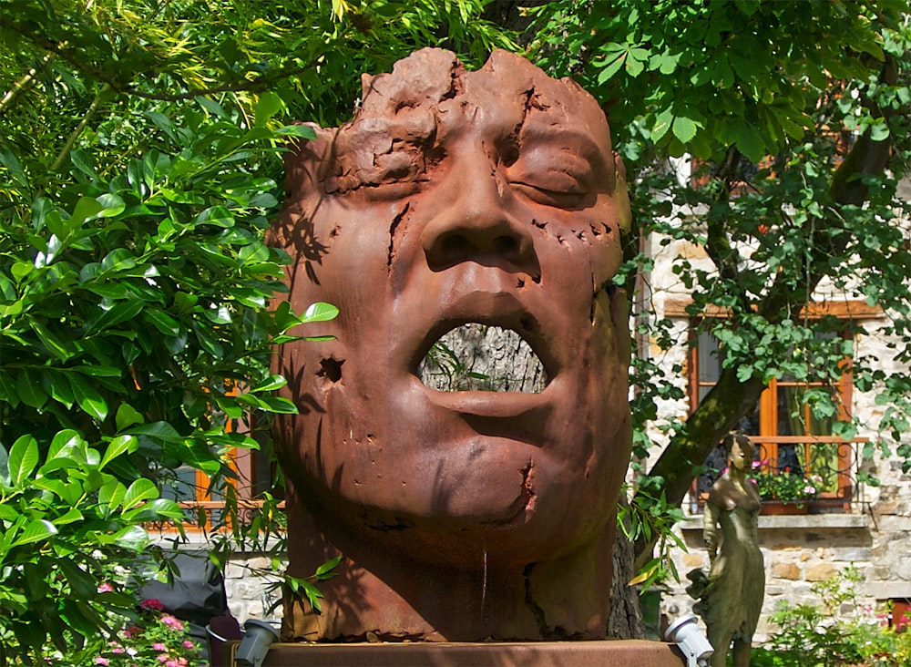 brown concrete face statue near green trees during daytime