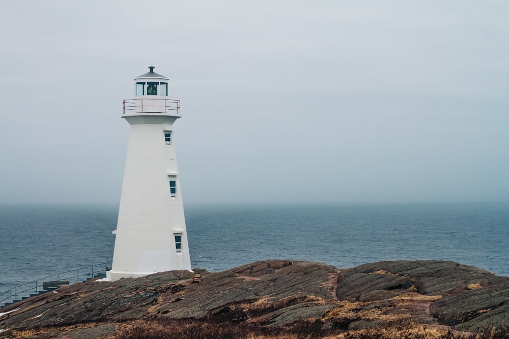 white and black lighthouse on brown rock formation near body of water during daytime