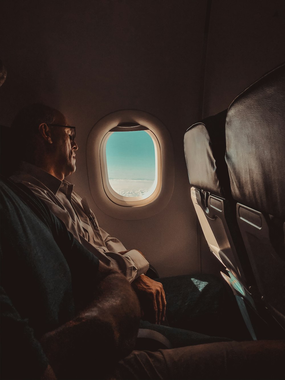 homme en veste noire assis sur un siège d’avion regardant la fenêtre pendant la journée
