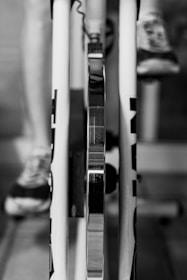 A close-up view of a bike trainer setup, showing the rear wheel mounted on the trainer with a focus on the metallic parts. One can see the leg of a person wearing sneakers, suggesting use for cycling or training indoors.