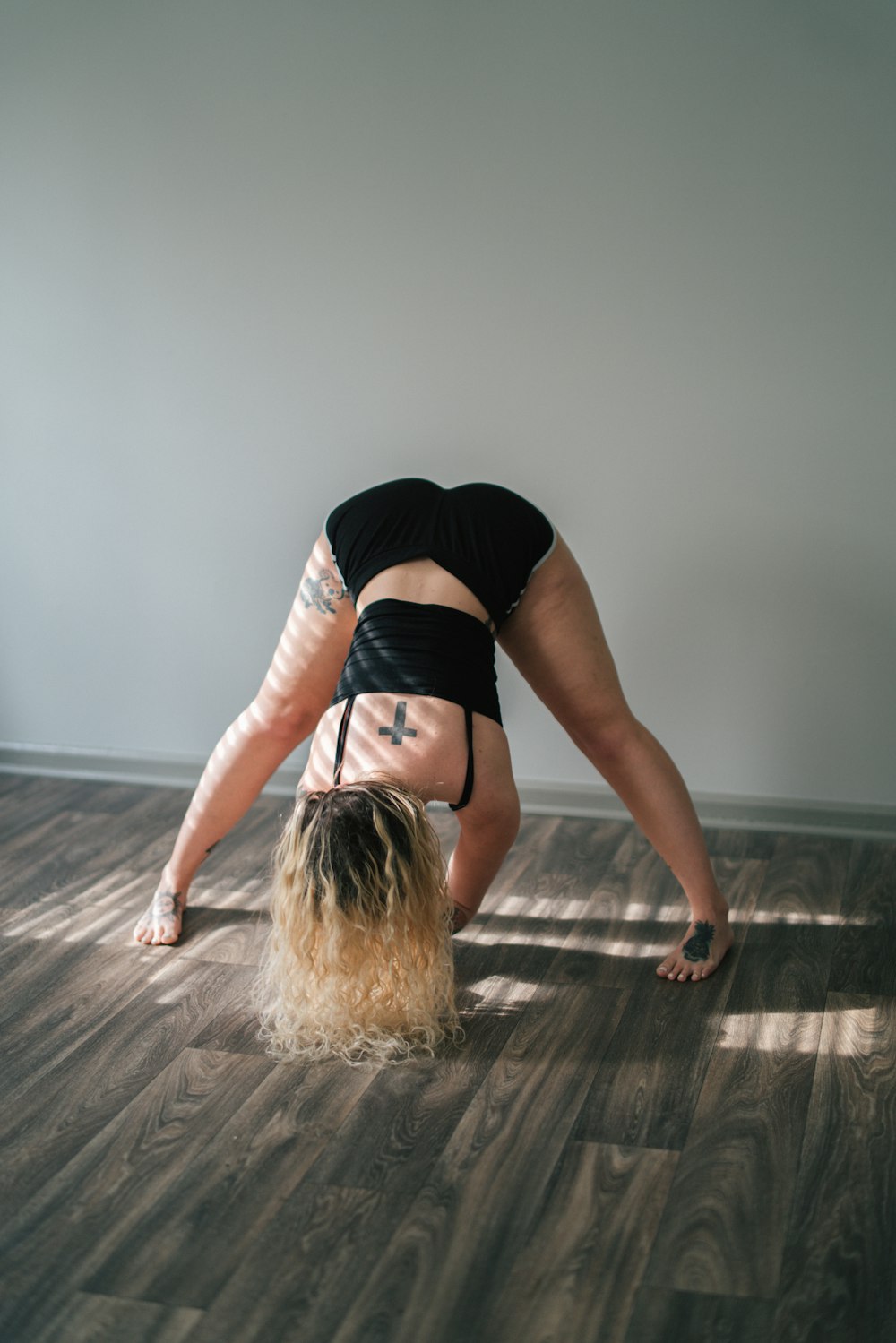 woman in black tank top and black shorts bending her body on brown wooden floor