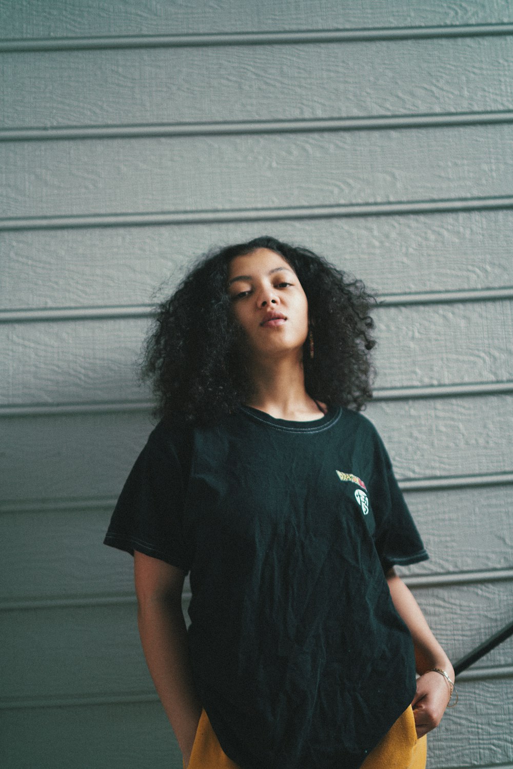 Femme en T-shirt à col rond noir debout à côté d’un mur gris