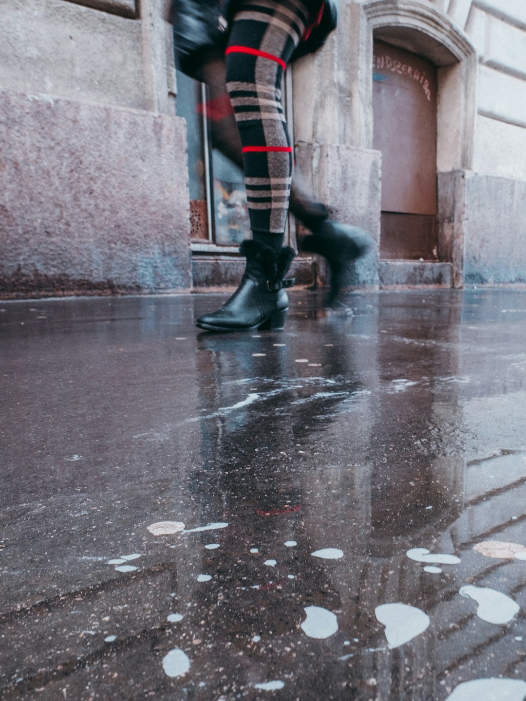 person in blue white and red striped pants and black boots walking on wet road