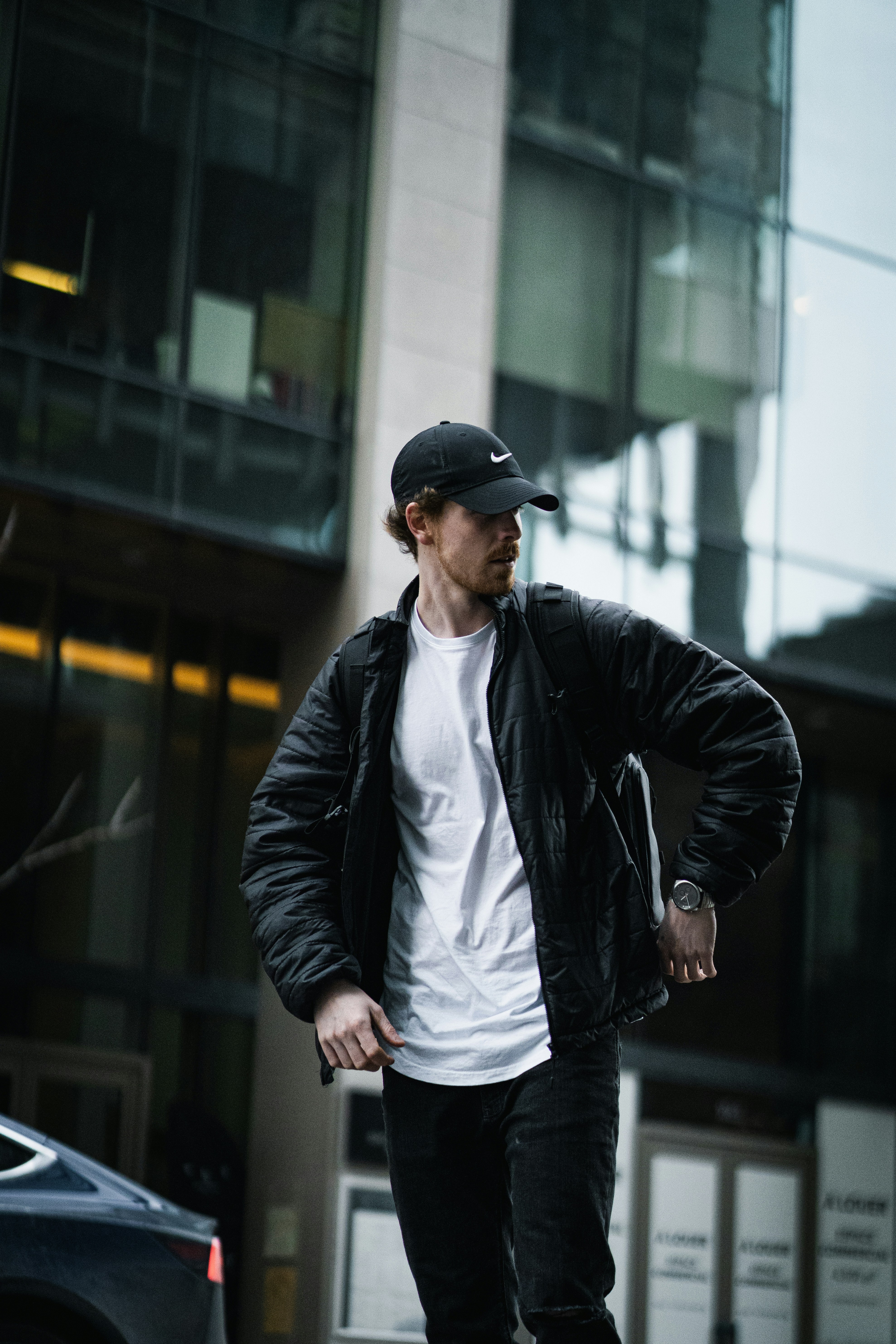 man in black leather jacket and black cap standing on sidewalk during daytime