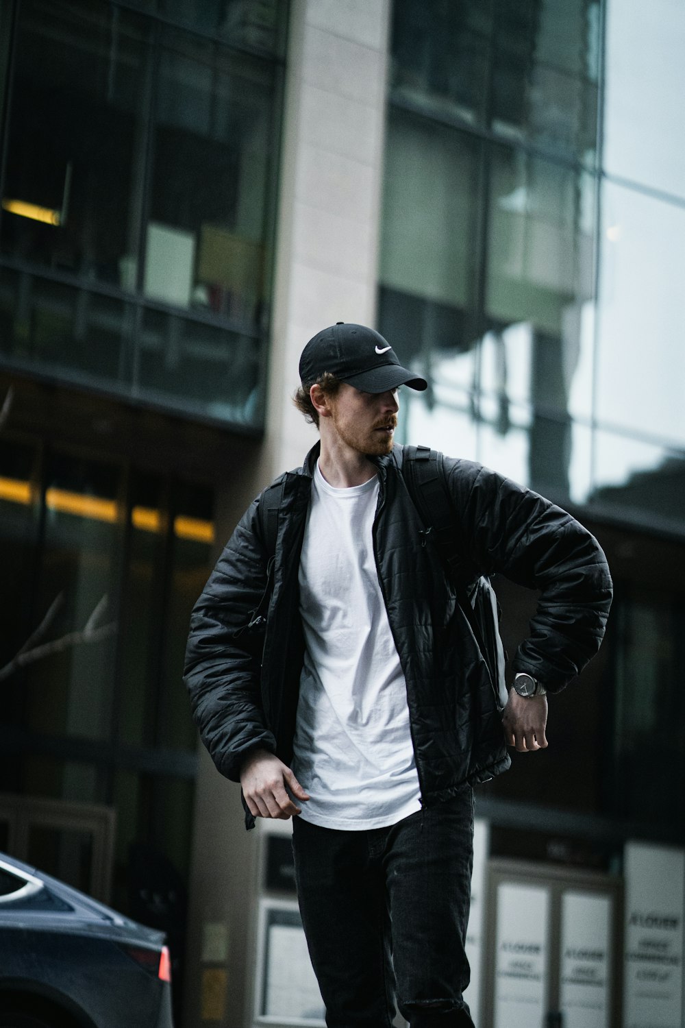 man in black leather jacket and black cap standing on sidewalk during daytime