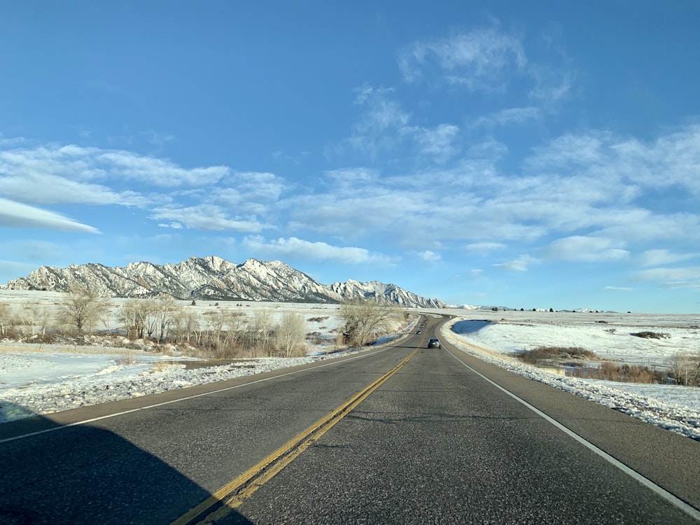 昼間は青空と白い雲の下、白い雪に覆われた山の近くの灰色のコンクリート道路