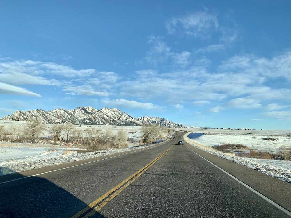 Route en béton gris près d’une montagne couverte de neige blanche sous un ciel bleu et des nuages blancs pendant la journée