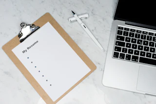 A clipboard holding a blank resume beside a fountain pen and a laptop keyboard.