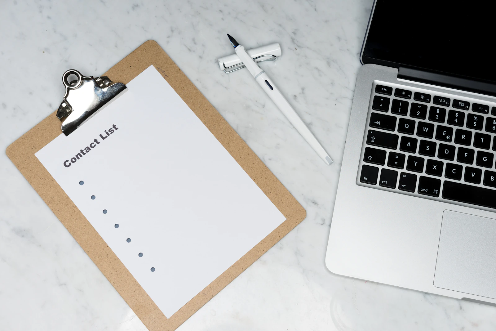 A clipboard with a list beside a laptop on a white marble desk