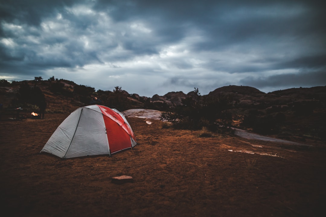 white and red dome tent on brown soil under gray clouds