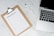 A clipboard with a paper titled 'Backpacking List' lies on a white marble surface. Beside it, there is a white pen and a laptop with a visible keyboard. The scene suggests organization or planning, possibly for a trip.