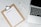A blank packing list on a clipboard is placed on a marble surface beside a pen and an open laptop.