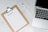 A blank packing list on a clipboard is placed on a marble surface beside a pen and an open laptop.