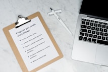 A marble surface displays a clipboard holding a paper with a list titled 'Projects you could start today!', placed next to an open laptop and a pen. The list suggests ideas like creating an online shop or a useful app.