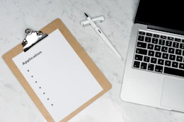 white paper on brown folder beside silver laptop computer
