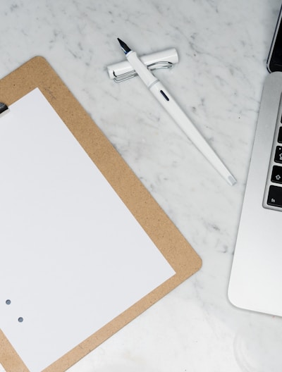 white paper on brown folder beside silver laptop computer