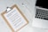 A clipboard with a paper titled 'Protective Measures #Covid19' lists safety guidelines. It includes steps such as washing hands, maintaining social distance, and seeking medical care early. Positioned on a marble surface, next to a silver laptop and a white pen.