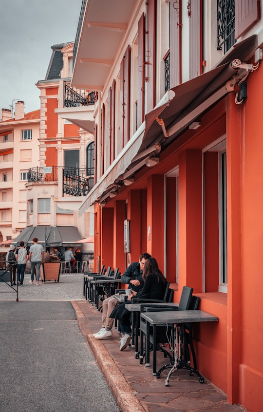 man in black jacket sitting on chair near red building during daytime in Saint-Jean-de-Luz France