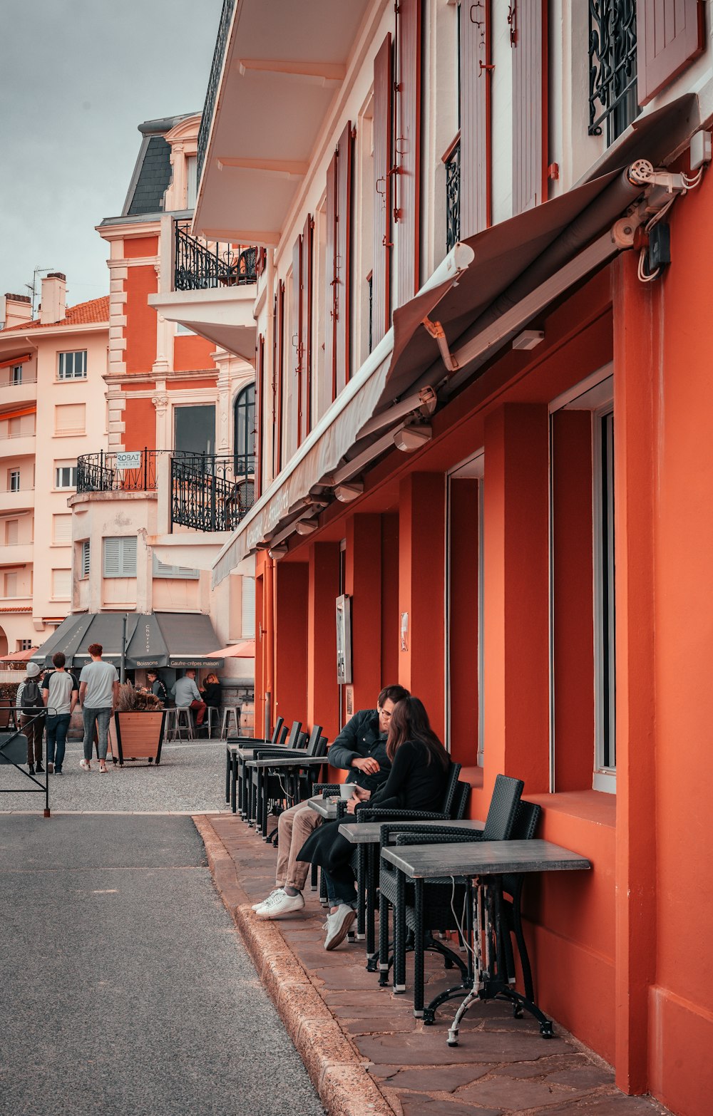 man in black jacket sitting on chair near red building during daytime