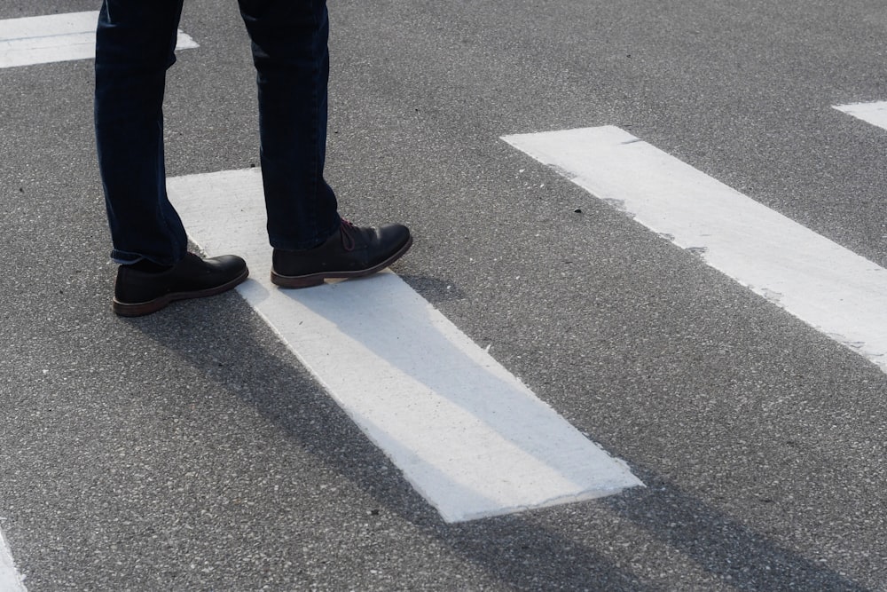 person in black pants and black shoes standing on gray asphalt road