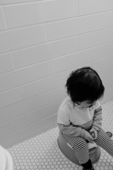 grayscale photo of child in white long sleeve shirt sitting on floor