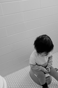 grayscale photo of child in white long sleeve shirt sitting on floor