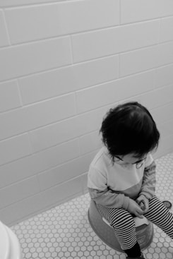 grayscale photo of child in white long sleeve shirt sitting on floor