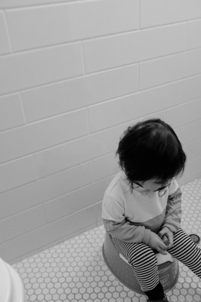 grayscale photo of child in white long sleeve shirt sitting on floor