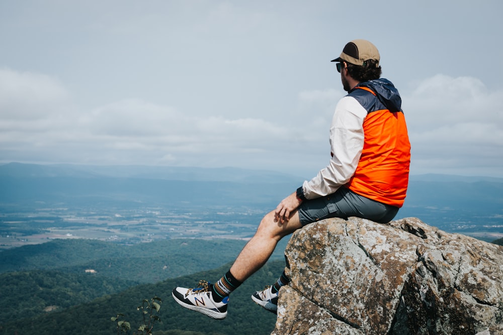 昼間、岩の上に座るオレンジ色のジャケットを着た男