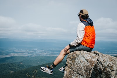 man in orange jacket sitting on rock during daytime virginia teams background