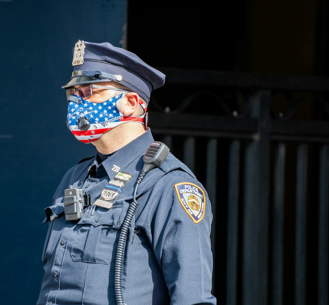 Side angle of an NYPD Officer wearing a patriotic American Flag themed N95 Ventilator Mask while on duty in New York City during the difficult period of Coronavirus policing.