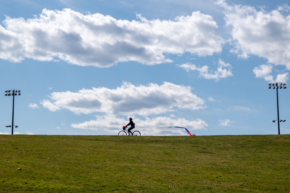 2 Männer fahren auf dem Fahrrad auf grünem Rasenplatz unter weißen Wolken und blauem Himmel während