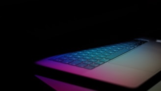 Close-up of a laptop keyboard with colorful backlighting in a dark room.