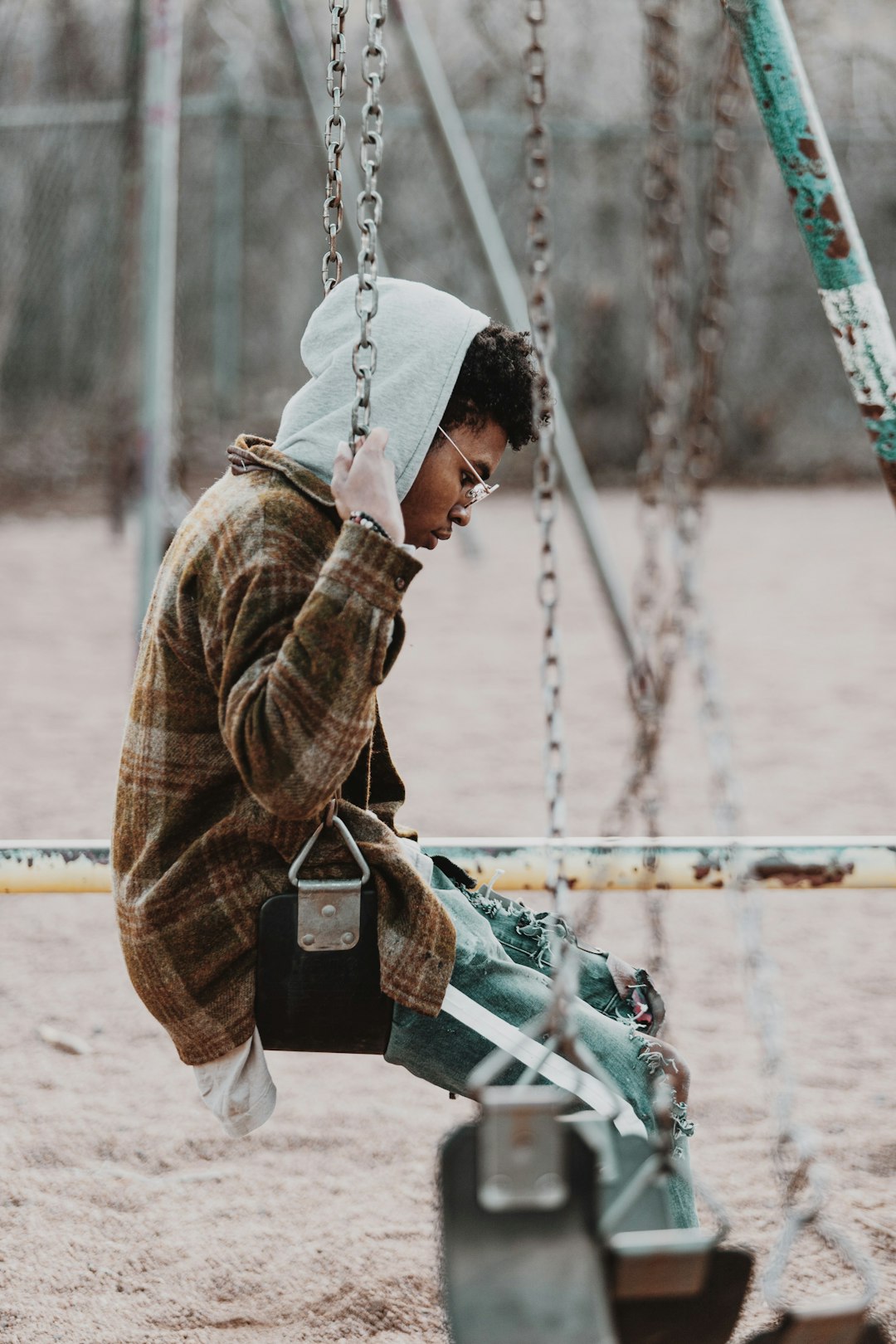 man in brown jacket and gray pants sitting on swing during daytime