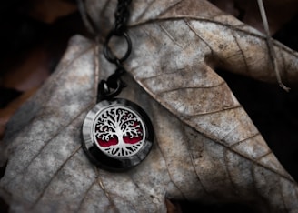 Handcrafted resin pendant with swirling black and silver patterns resting on a bed of moss and autumn leaves.