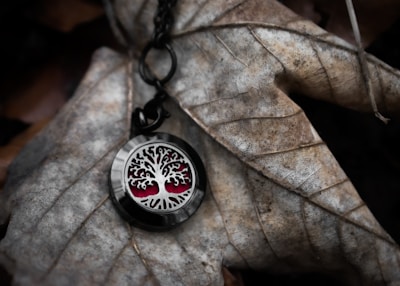 Handcrafted resin pendant with swirling black and silver patterns resting on a bed of moss and autumn leaves.