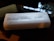 A white oblong container with horizontal ridges on its surface has the words 'Random Useful Bits' handwritten on it in black ink. The container is placed on a dark, reflective surface near a window, allowing natural light to illuminate the scene.
