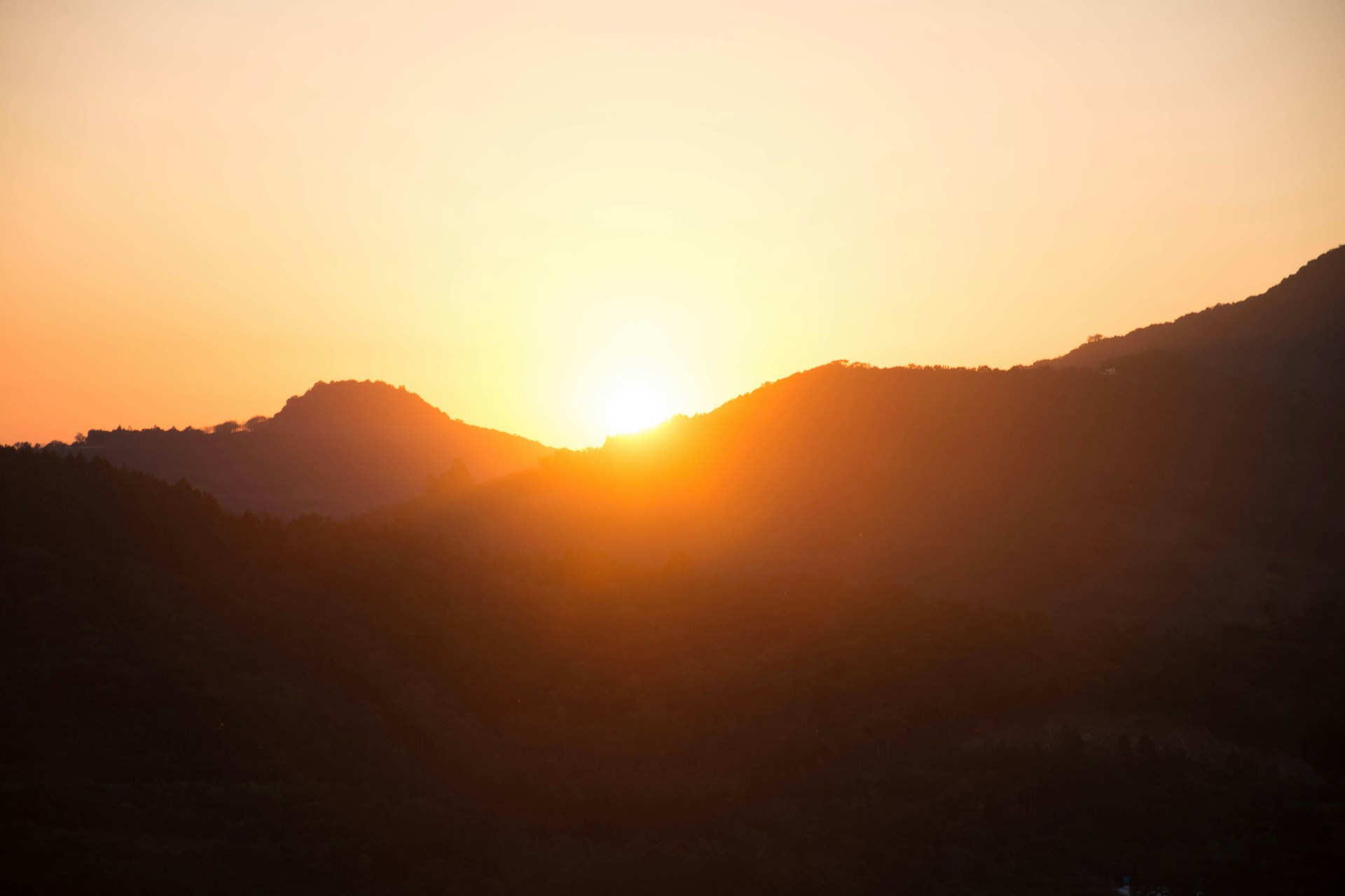 Golden sunlight breaking over the horizon, illuminating the silhouette of Mount Batur and the shimmering Lake Batur below.