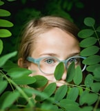 girl in blue framed eyeglasses hiding behind green leaves